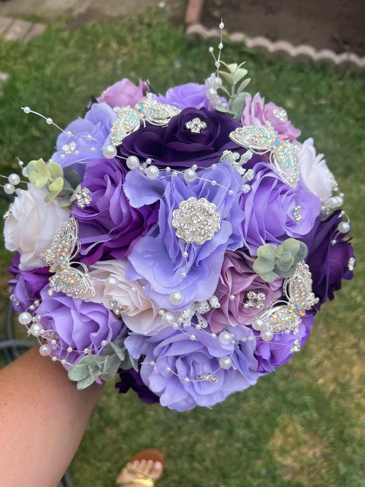 a bridal bouquet with purple flowers and jewels on the bride's wrist is shown from above