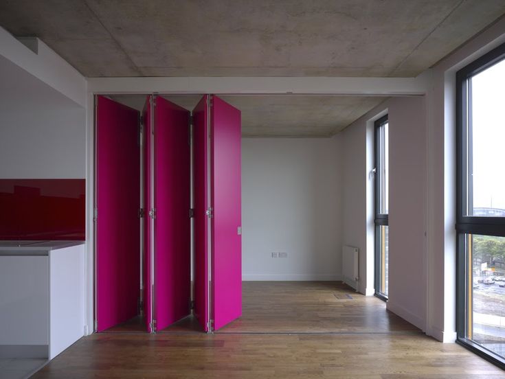 an empty room with pink partitions on the wall and wood flooring in front of large windows