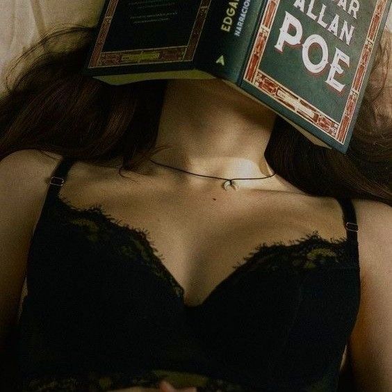 a woman laying in bed with an open book on her head over her face, reading allian poe