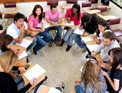 a group of people sitting at desks in a circle with notebooks on their laps