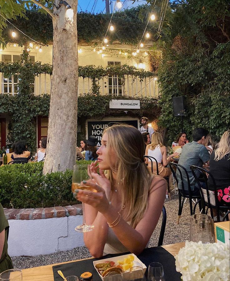 a woman sitting at a table with food in front of her and people eating outside