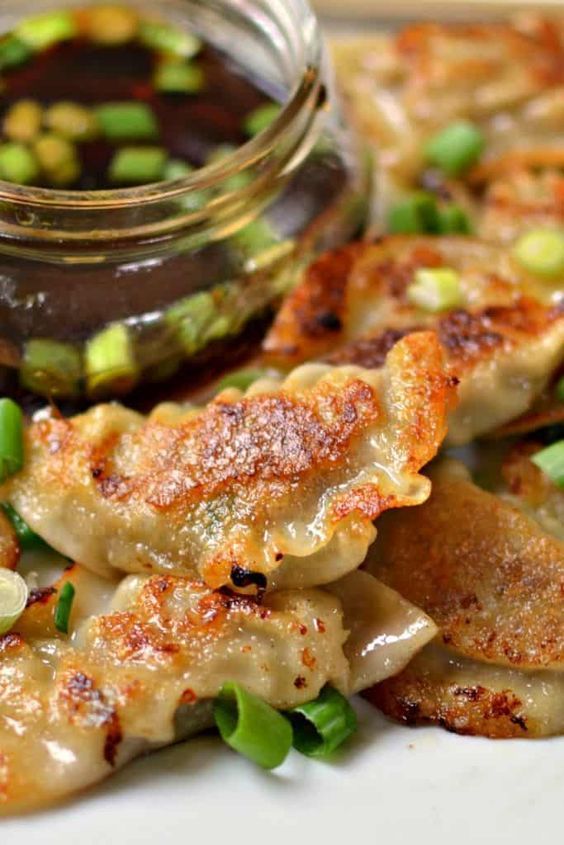 some food that is on a plate with sauce and green onions next to it in a glass jar