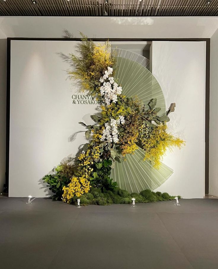 an art piece with flowers and leaves on display in front of a large screen wall