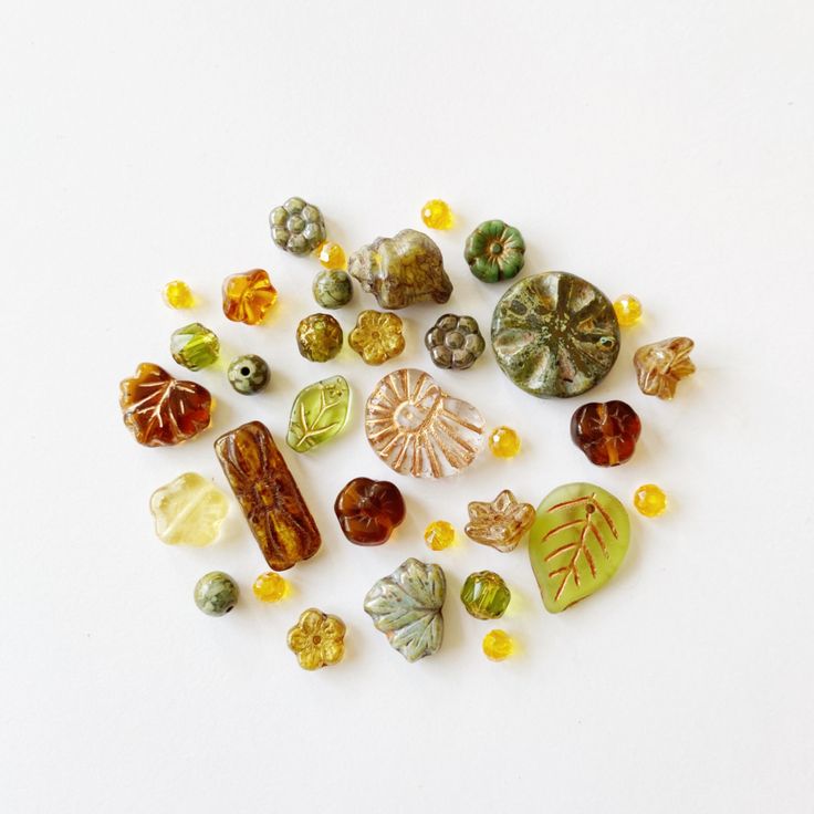 several different types of glass beads on a white surface, including leaves and acorns