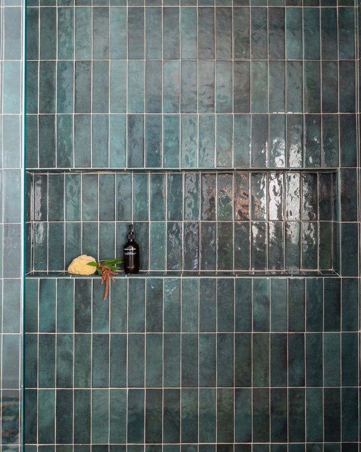 a green tiled wall with a bottle and toothbrush on it