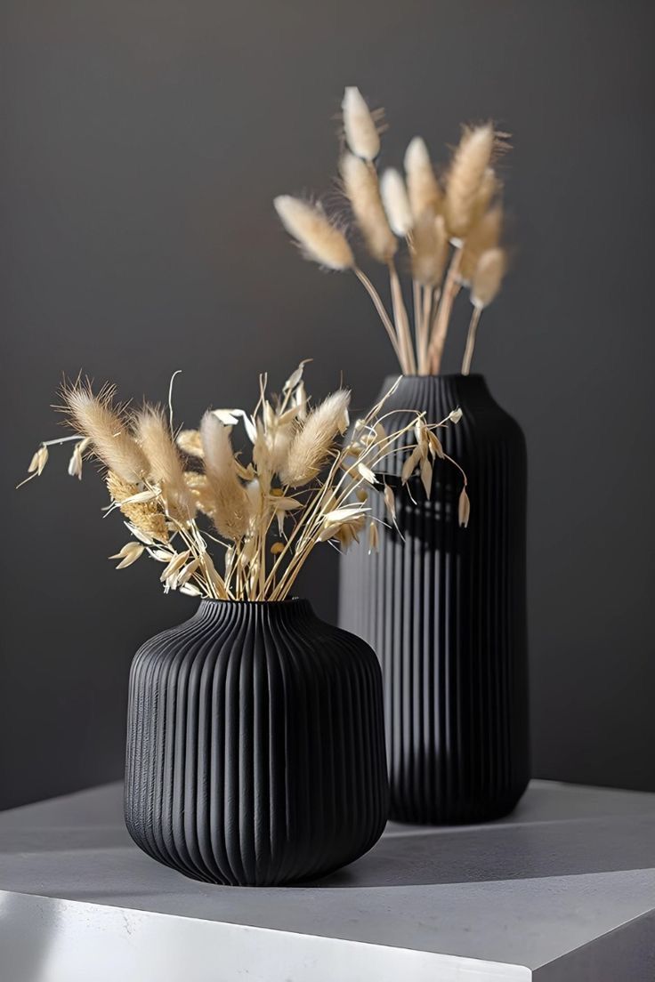 two black vases with dried plants in them