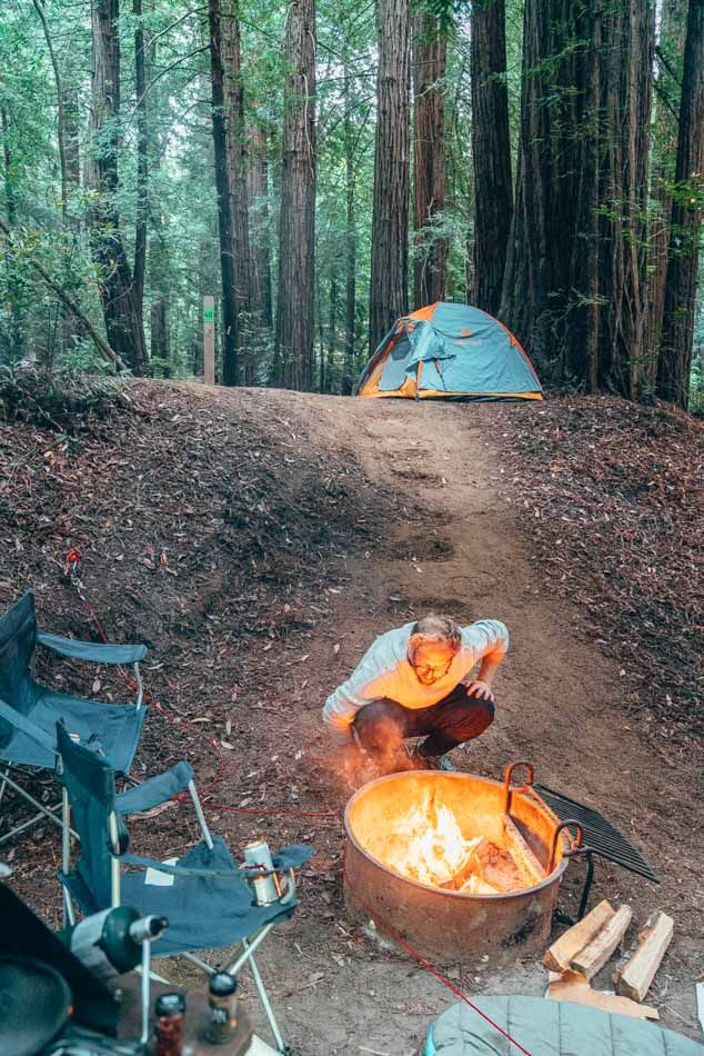 two tents set up in the woods next to a campfire with a person cooking over it