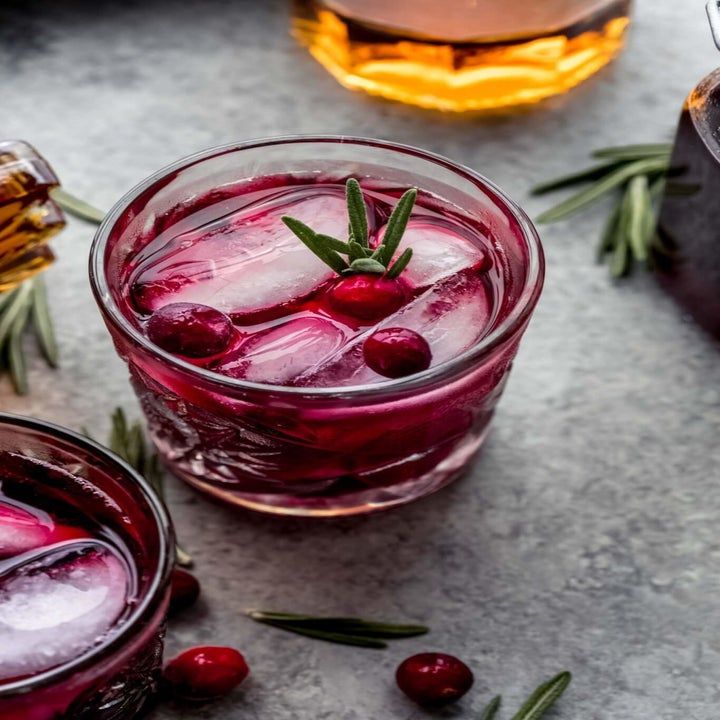 two glasses filled with ice and cranberry juice on top of a gray surface