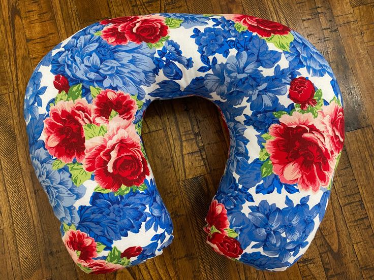 a blue and red flowered neck pillow sitting on top of a wooden floor next to a pair of scissors