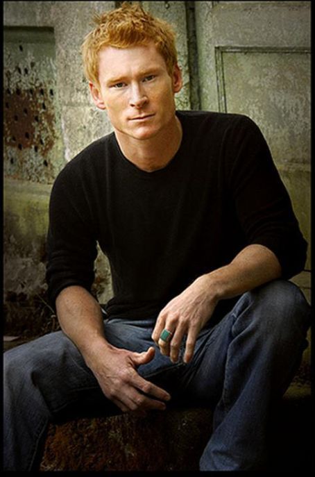 a man sitting on top of a wooden bench next to a wall with peeling paint