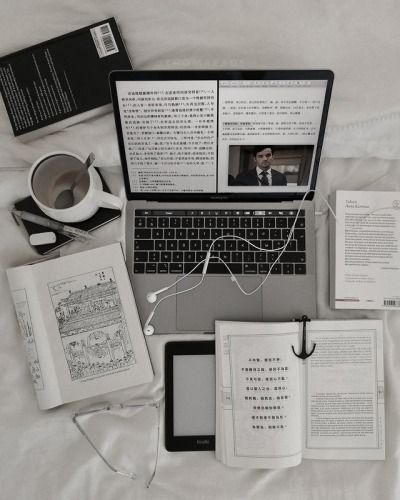 an open laptop computer sitting on top of a bed next to books and other items