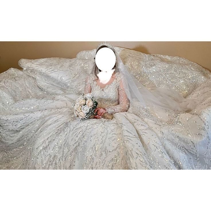 a woman sitting on top of a bed covered in a white dress and holding a bouquet