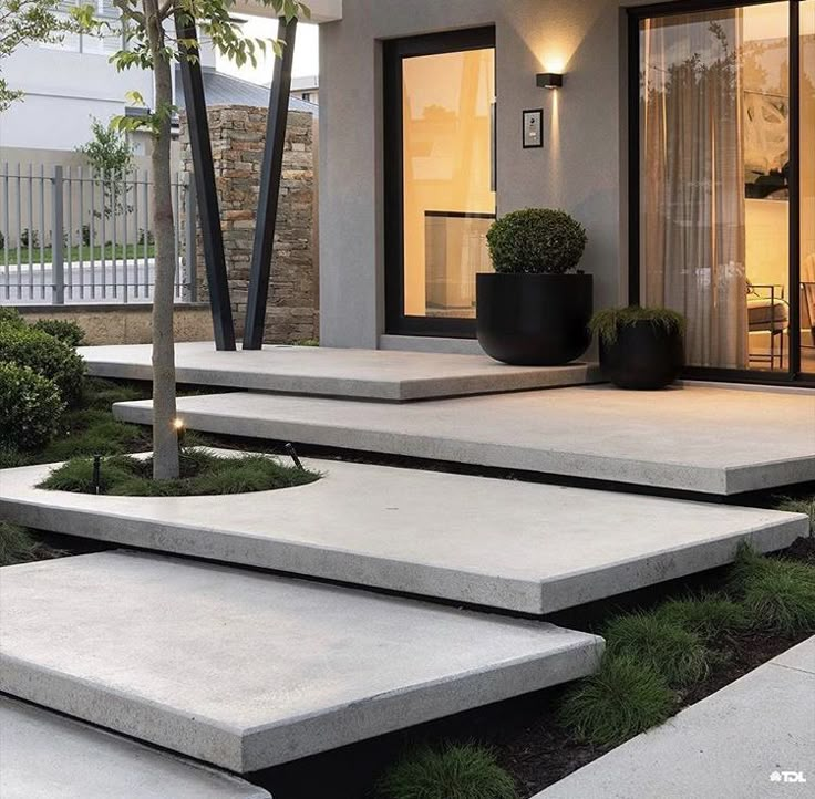 modern concrete steps leading up to the front door of a house with potted trees