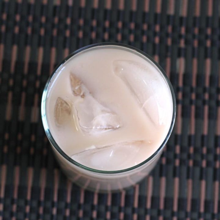 a glass filled with ice sitting on top of a wooden table next to a black mat