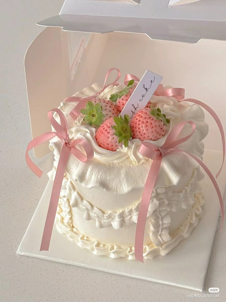 a white cake with strawberries on top and pink ribbon around the edges in a box