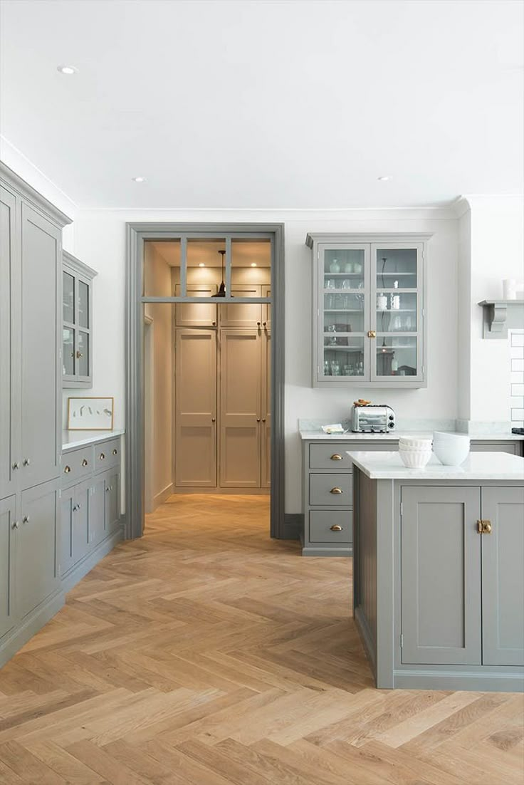 a large kitchen with wooden floors and gray cabinetry on the walls, along with white counter tops