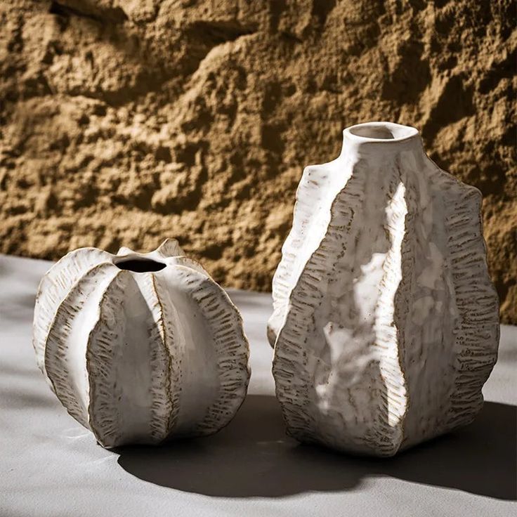 two white vases sitting next to each other on top of a cloth covered table