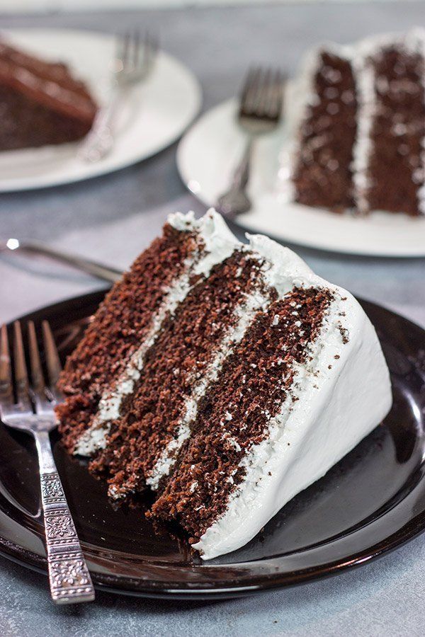 a slice of chocolate cake with white frosting on a plate next to a fork