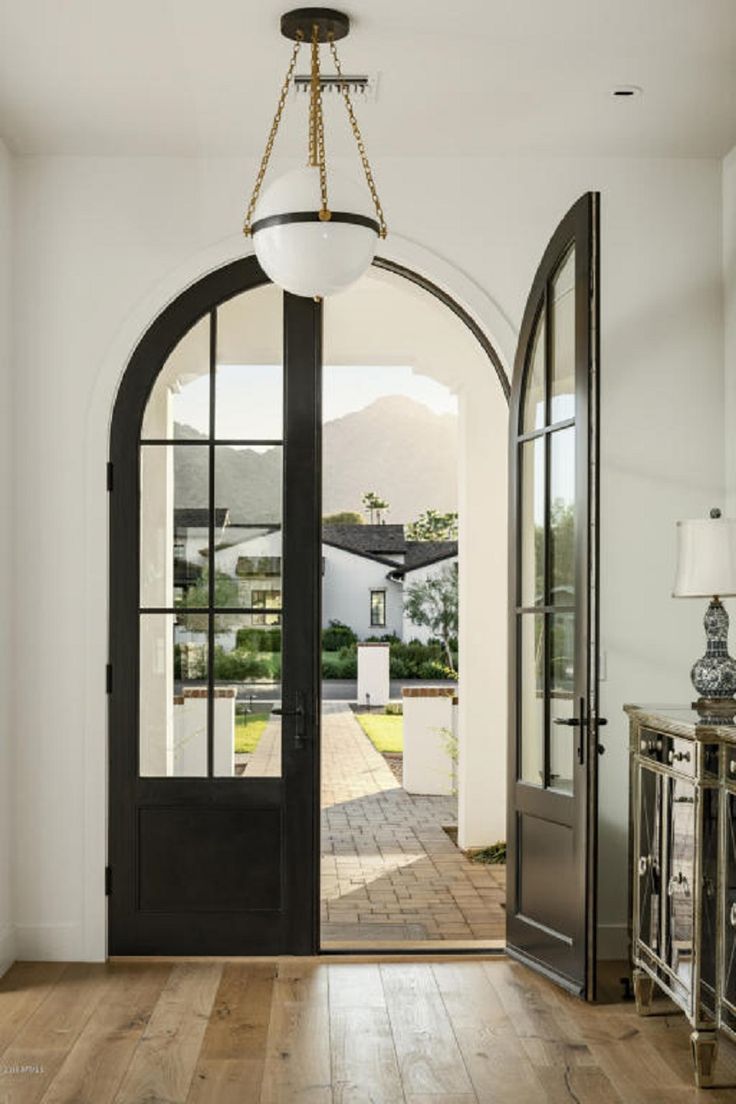 an open door leading into a large room with wooden floors and white walls, along with a chandelier hanging from the ceiling