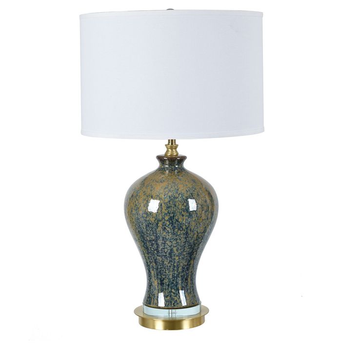 a green and gold lamp with a white shade on the top is sitting against a white background