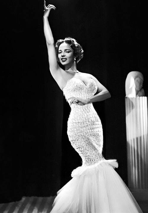 a black and white photo of a woman in a dress with her hand up to the sky