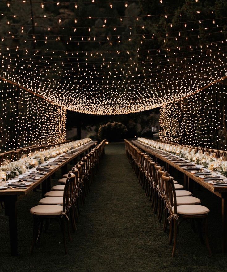 a long table set up for dinner with lights on the ceiling and chairs around it