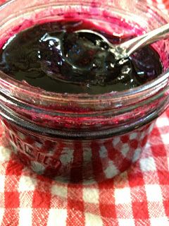 a jar filled with blueberry jam on top of a checkered table cloth