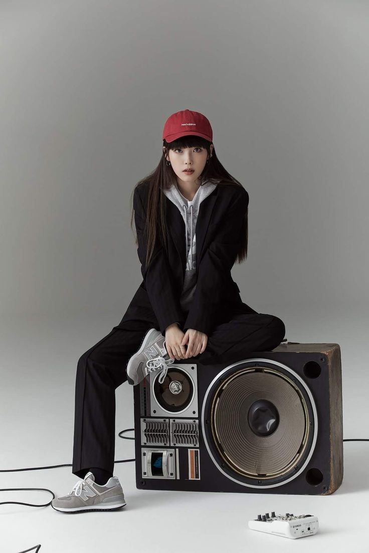 a woman sitting on top of a boombox with headphones around her neck and wearing a red hat