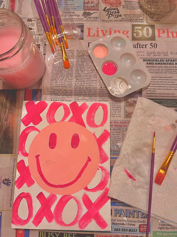 an image of a smiley face painted on newspaper with paintbrushes and other art supplies