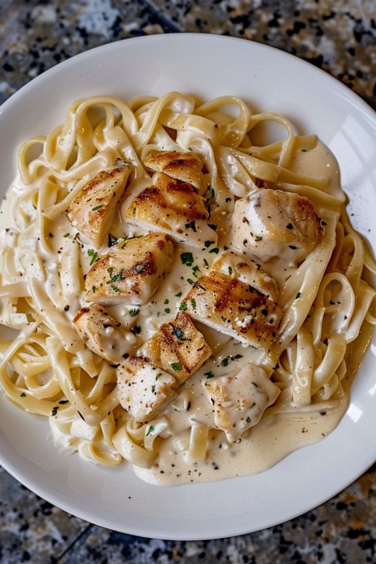 a white plate topped with pasta covered in sauce and chicken breast pieces on top of it