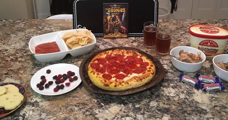 a pizza sitting on top of a table next to bowls of fruit and crackers