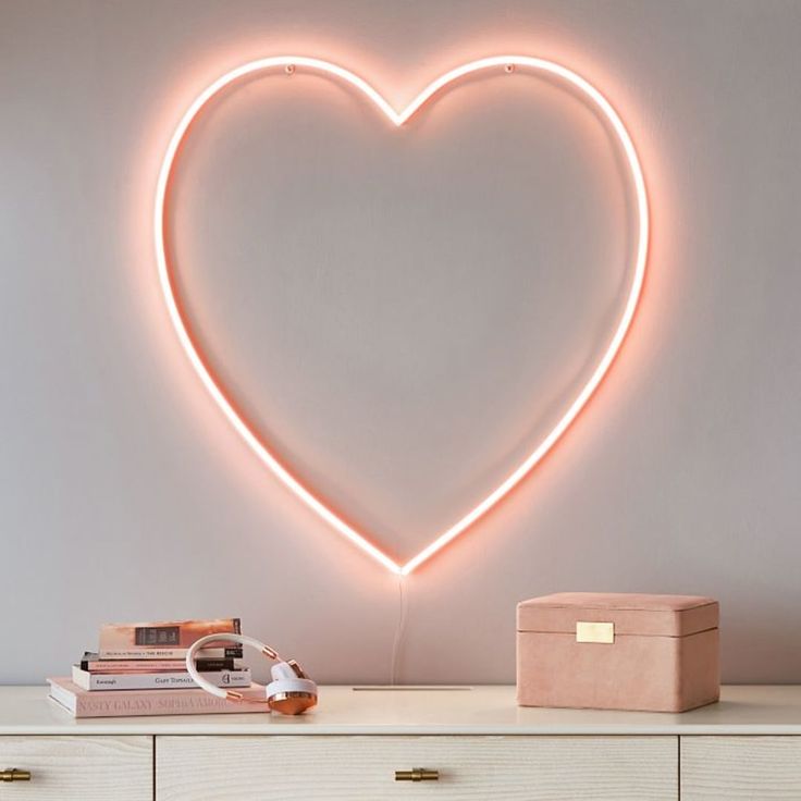 a heart - shaped neon sign on the wall above a dresser with books and a box