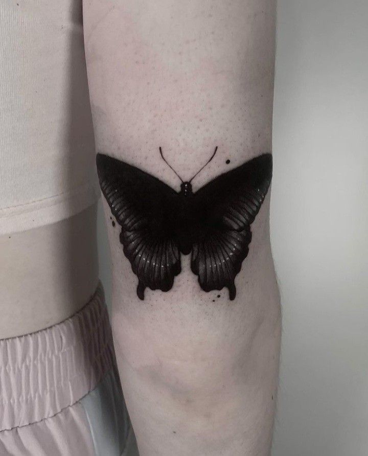 a small black butterfly tattoo on the right leg, it looks like an insect with wings spread