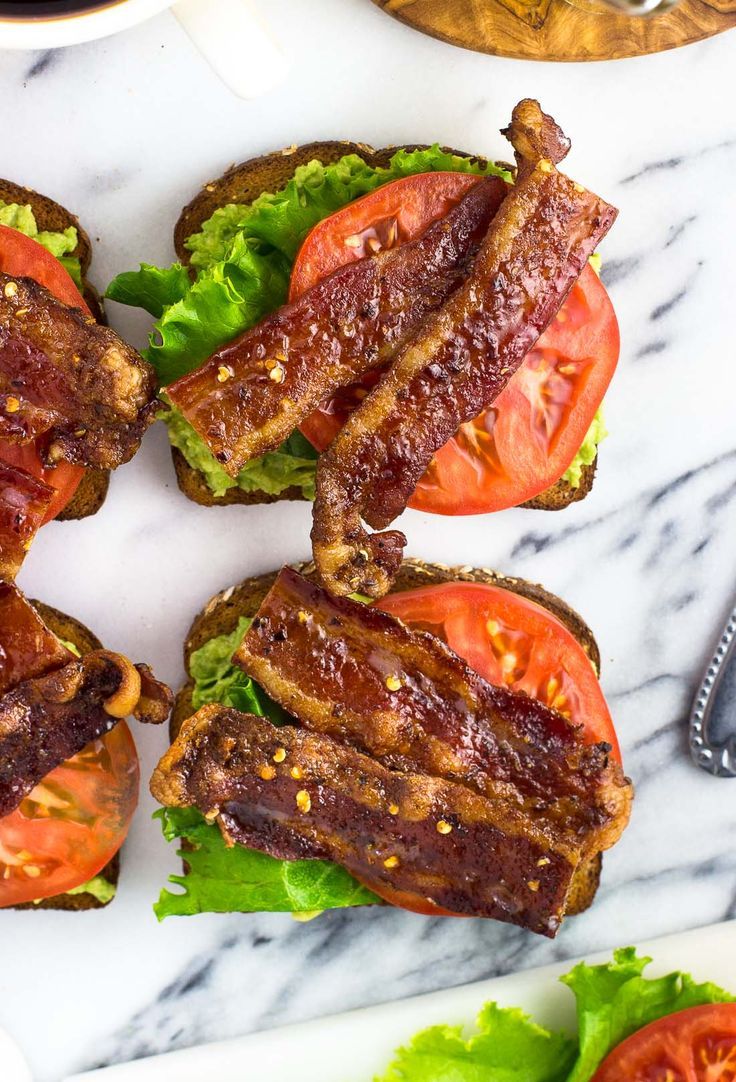 bacon wrapped in lettuce and tomato slices on a marble counter top with silverware