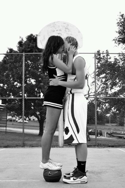 two people standing on a basketball court with an umbrella over their heads and one person kissing the other