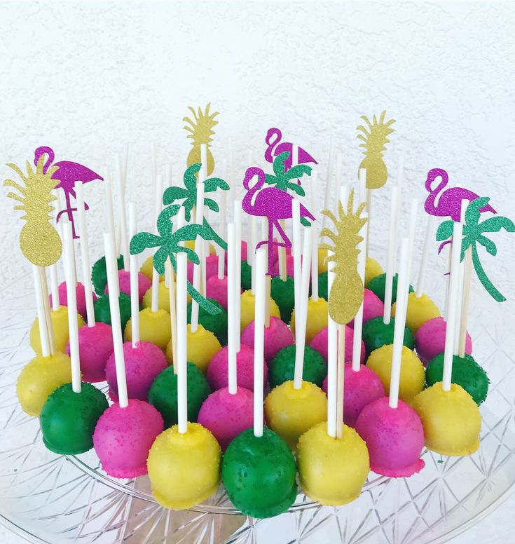 cake pops decorated with pink, yellow and green frosting are on a clear plate