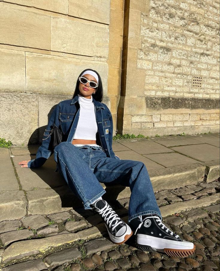 a woman sitting on the steps with her legs crossed wearing jeans and white shirt, black converse sneakers