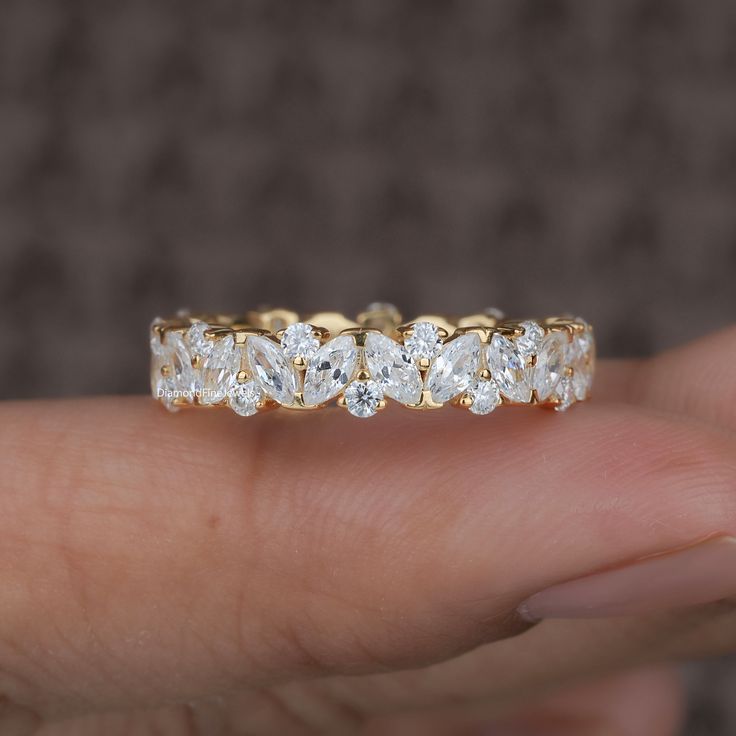 a woman's hand holding a yellow gold ring with five diamonds on it,