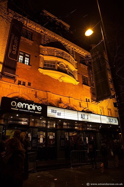 the front of an old theater at night with people standing outside and on the sidewalk