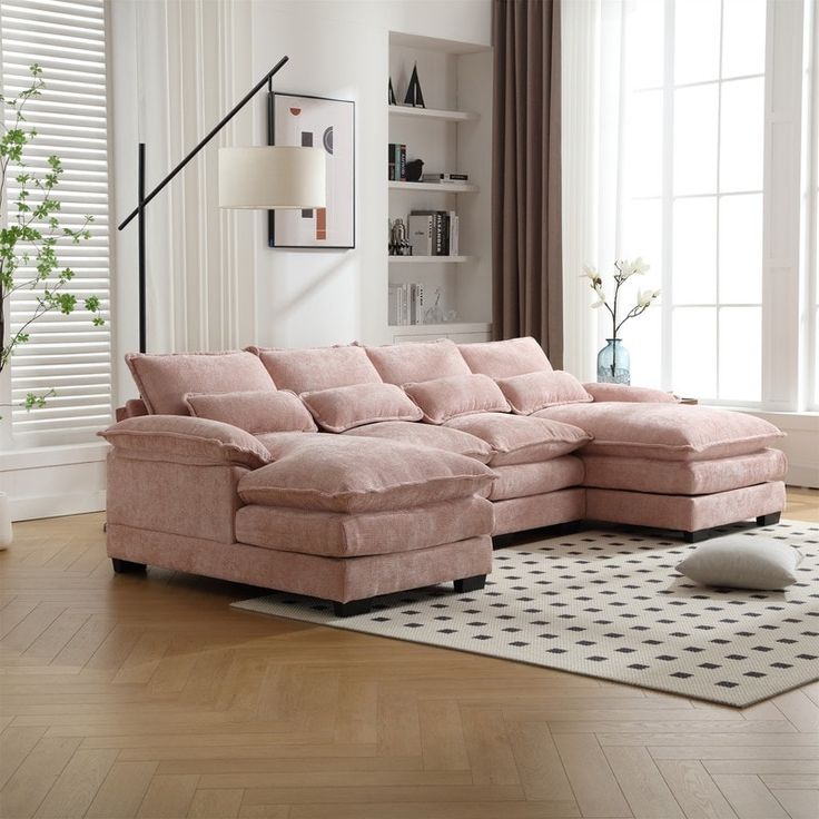 a living room with a large pink sectional couch and white rug on the wooden floor