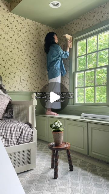 a woman standing in front of a window next to a bed