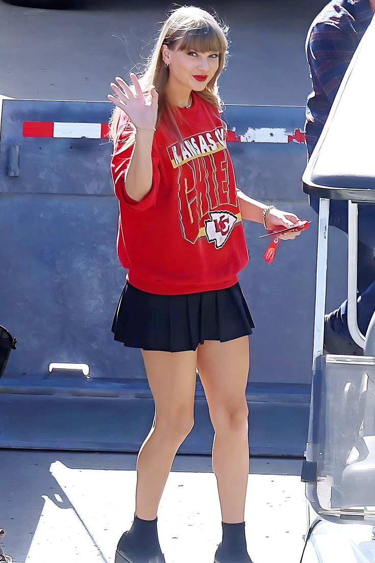 taylor swift is wearing a red shirt and black skirt as she steps out of her car