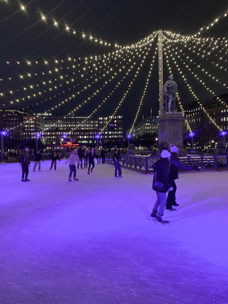 people skating on an ice rink at night with lights strung over the bridge and buildings in the background