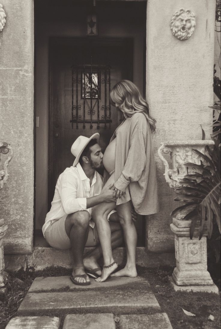 black and white photograph of a man kneeling down to his pregnant wife in front of a door