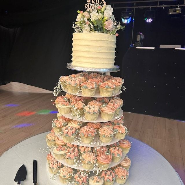 a wedding cake with cupcakes and flowers on the top tier in front of a crowd