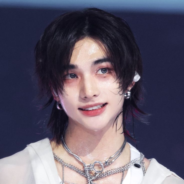 a man with black hair wearing a white shirt and silver jewelry on his neck is looking at the camera