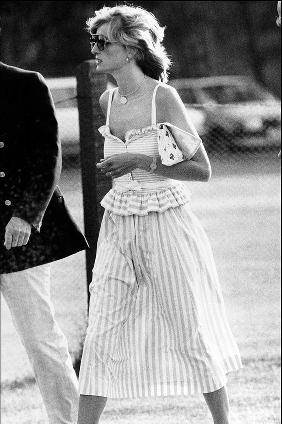 black and white photograph of woman in striped dress walking with man behind her wearing sunglasses