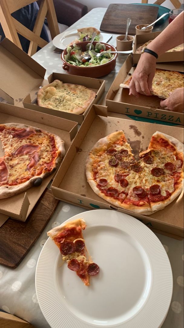 several pizzas in boxes on a table with plates and utensils around them