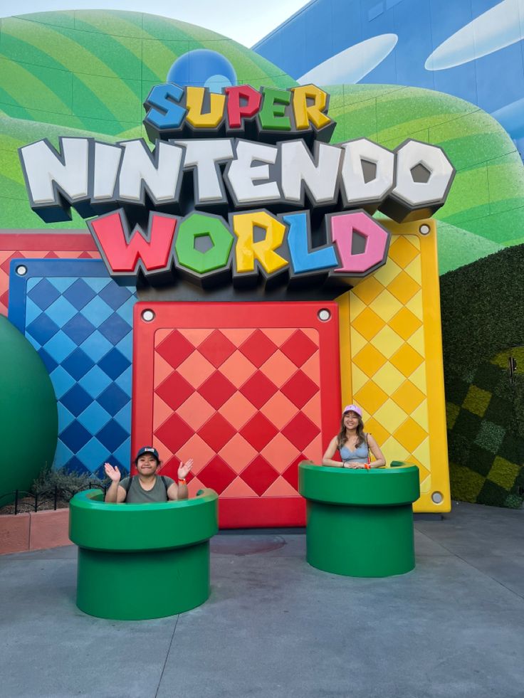 two people are sitting on green chairs in front of the entrance to super nintendo world