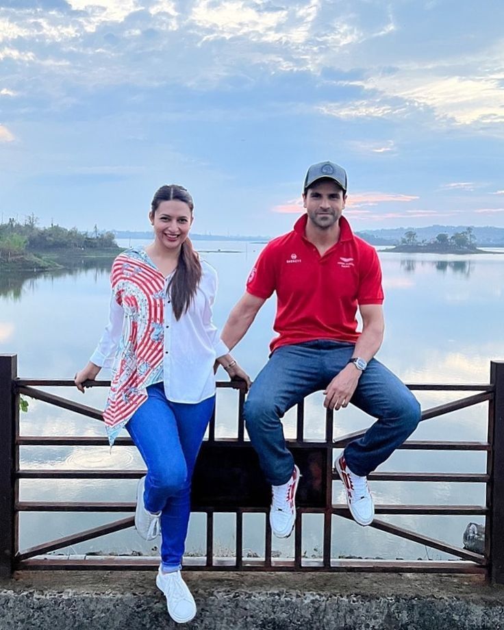 a man and woman sitting on top of a metal fence next to a body of water